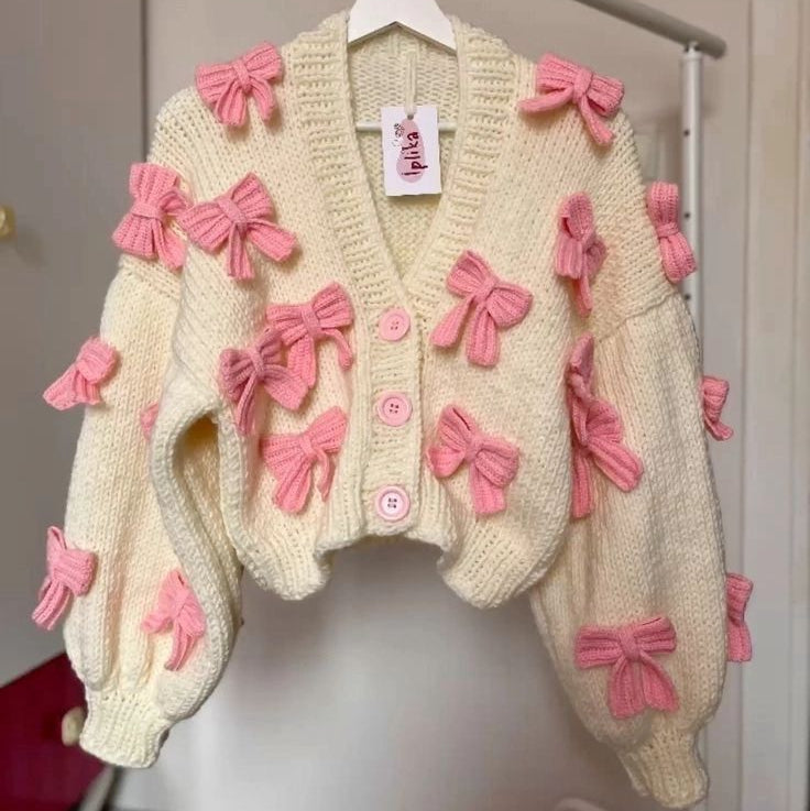Beige cardigan with pink bows hanging on a rack