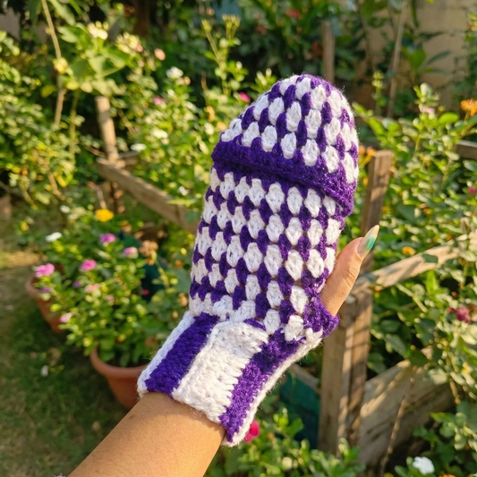 Purple and white crocheted gardening glove held in front of a garden background.