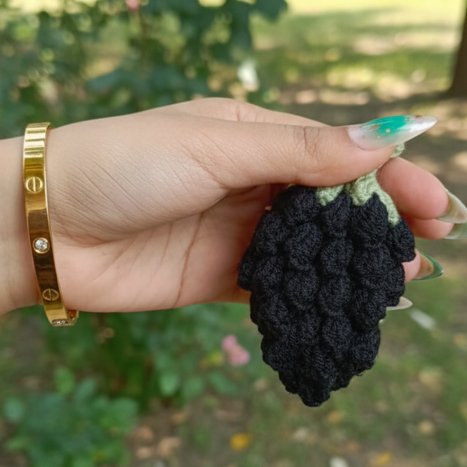 Hand holding a blackberry with a blurred green outdoor background