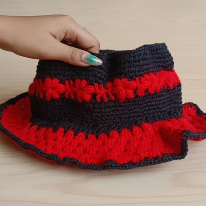 Hand holding a red and black crocheted bag on a wooden surface