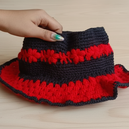 Hand holding a red and black crocheted bag on a wooden surface